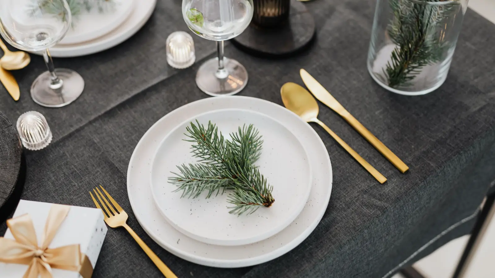 Gold cutlery and white plates on a dark linen table set for a festive dinner