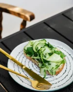 Aurelle gold fork and knife on a dotted plate with cucumber toast on a dark wooden table