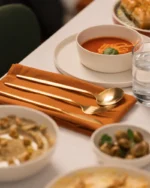 Aurelle gold cutlery on terracotta napkins at a dinner table set with soups and small plates