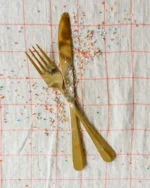 Aurelle gold fork and knife crossed on a pastel checked tablecloth with colourful sprinkles