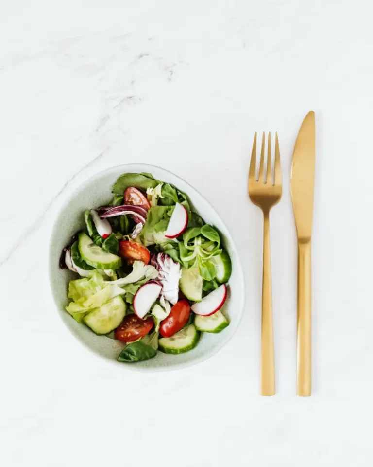 Aurelle gold fork and knife beside a fresh vegetable salad on a white marble table