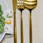 Close-up of the Aurelle gold cutlery set: dinner knife, fork and spoon on a linen napkin