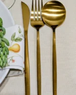 Close-up of the Aurelle gold cutlery set: dinner knife, fork and spoon on a linen napkin