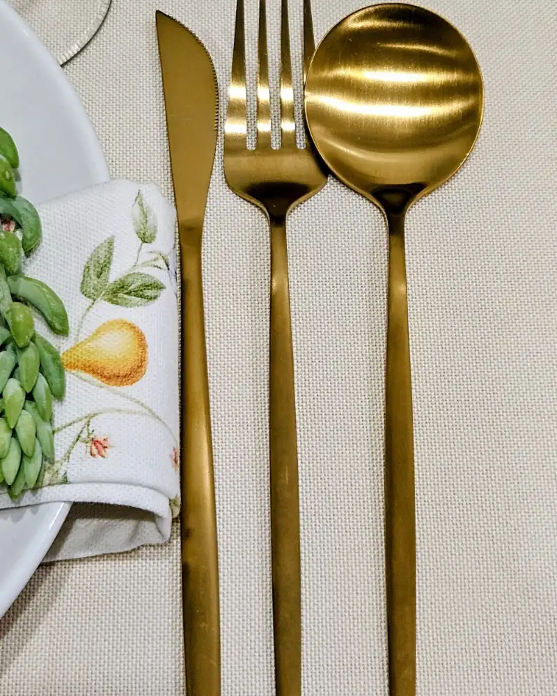 Aurelle gold cutlery close-up Close-up of the Aurelle gold cutlery set: dinner knife, fork and spoon on a linen napkin