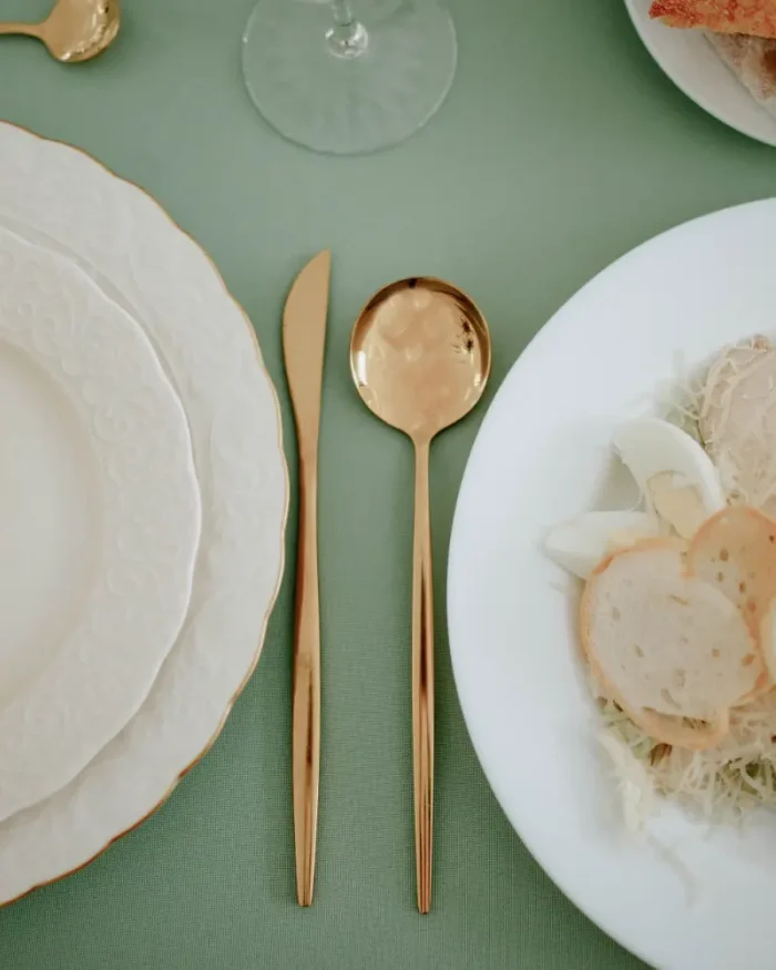 Aurelle gold knife and spoon between white scalloped plates on a sage green table