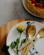 Aurelle gold spoons on a ceramic plate next to a berry cake and a yellow rose