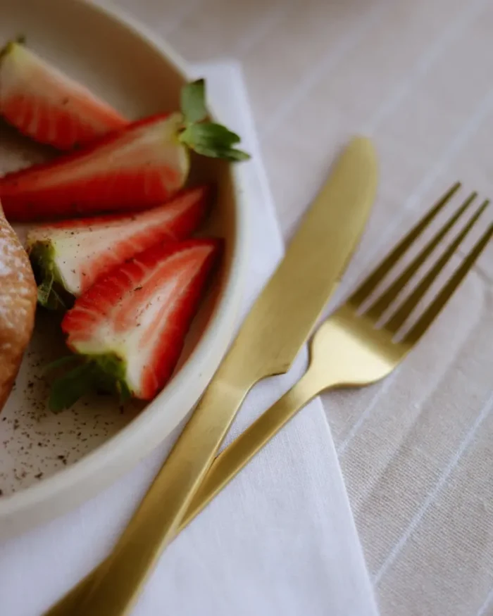 Aurelle gold knife and fork beside fresh strawberries on white linen