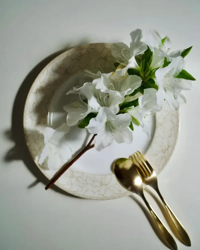 Aurelle gold fork and spoon on a patterned plate styled with white azalea flowers