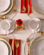 Overhead view of a festive table set with gold-rimmed white plates, cups, gold cutlery and red napkins