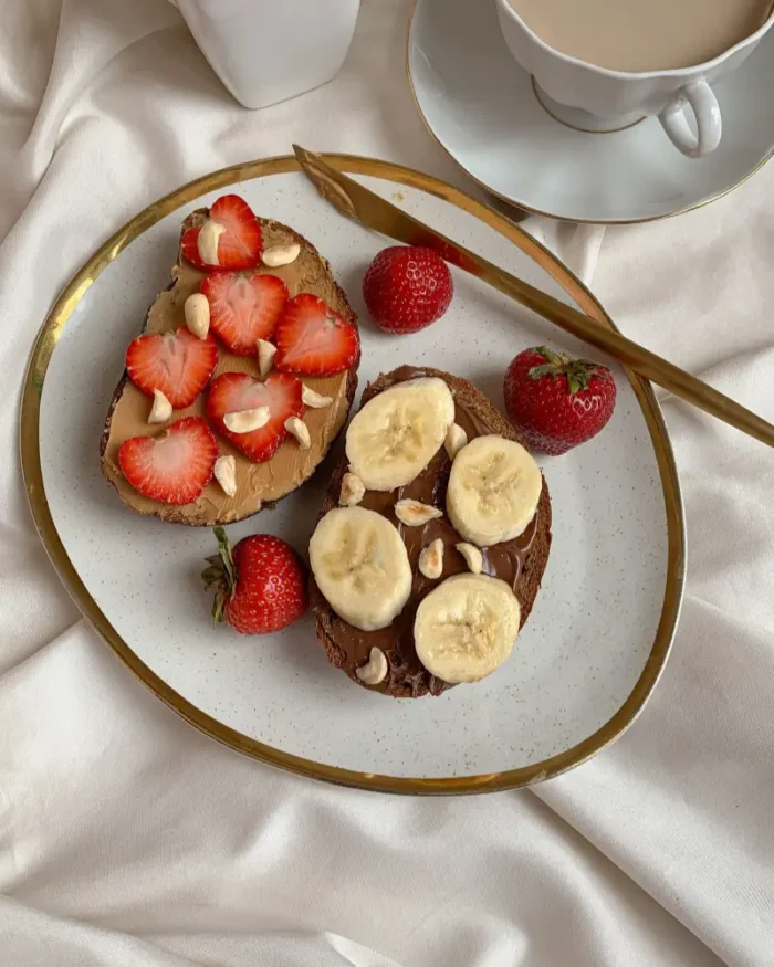 Gold-rimmed ceramic plate serving fruit toast with strawberries and banana on cream linen