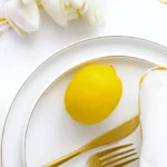 White porcelain dinner plate with a fine gold rim, styled with a lemon and gold cutlery on white linen