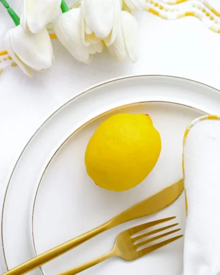 White porcelain dinner plate with a fine gold rim, styled with a lemon and gold cutlery on white linen