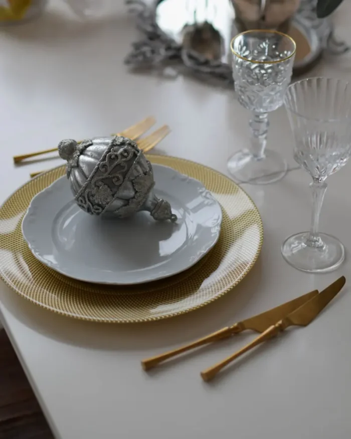White dinner plate on a gold charger with gold cutlery and crystal glasses in an elegant table setting