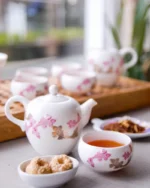 Camellia porcelain teapot and teacups with pink floral detail served with biscuits