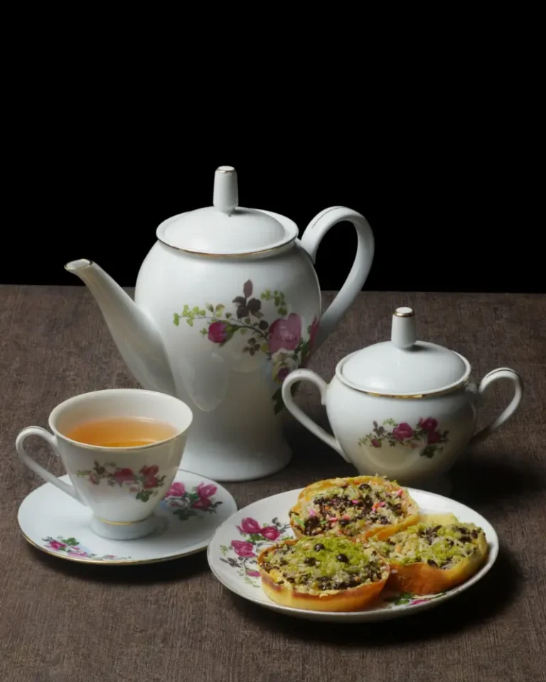 Camellia porcelain teapot, sugar bowl and teacup with saucer beside a plate of snacks