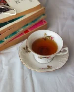 Camellia porcelain teacup and saucer of tea on white bedding beside a stack of books
