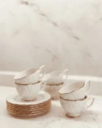 Camellia white porcelain teacups and saucers with gold rims on a marble surface