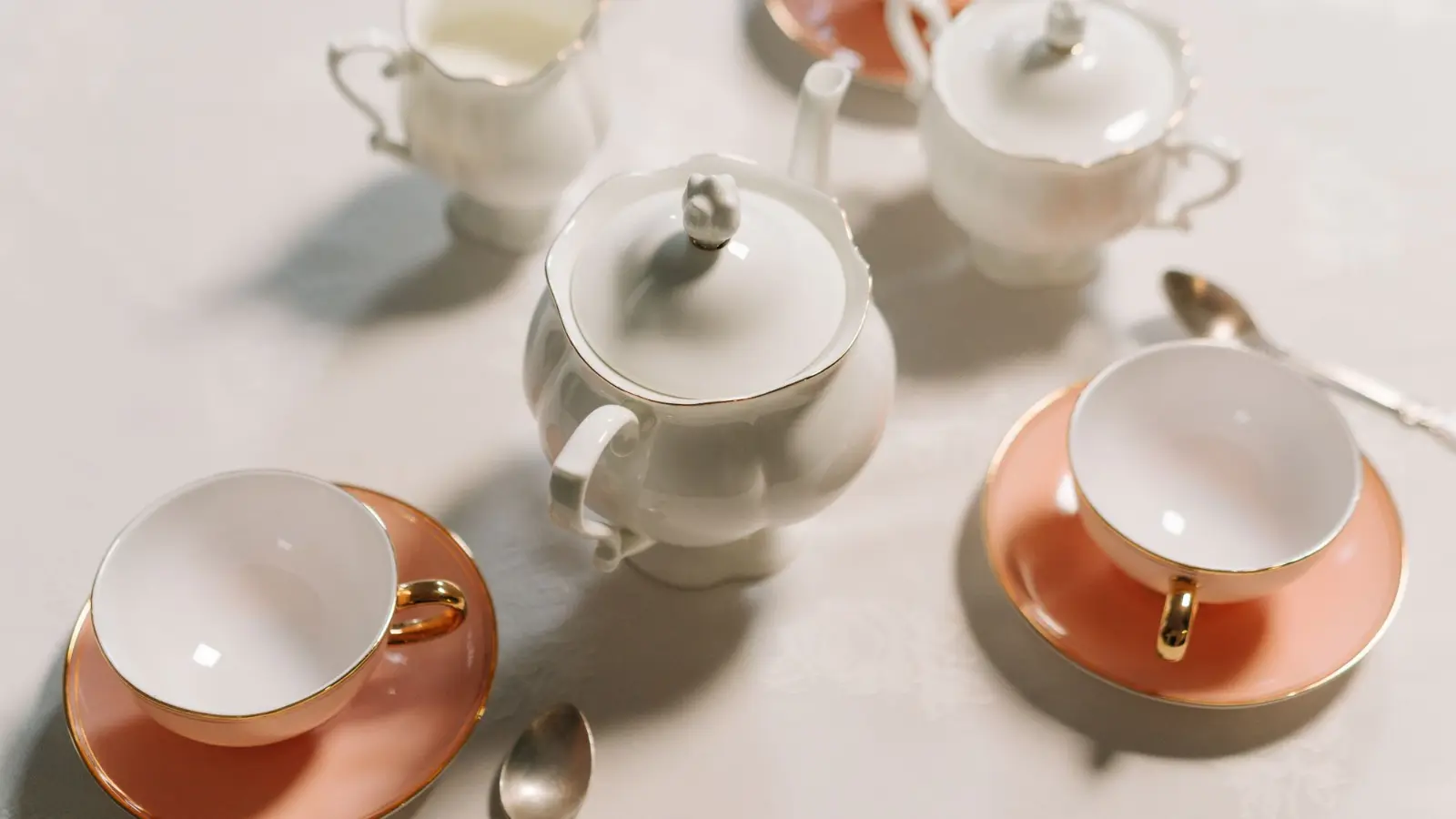 White porcelain teapot with blush pink teacups and saucers set for afternoon tea