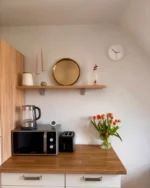 Halo minimal wall clock above a wooden kitchen shelf with a toaster, microwave and tulips