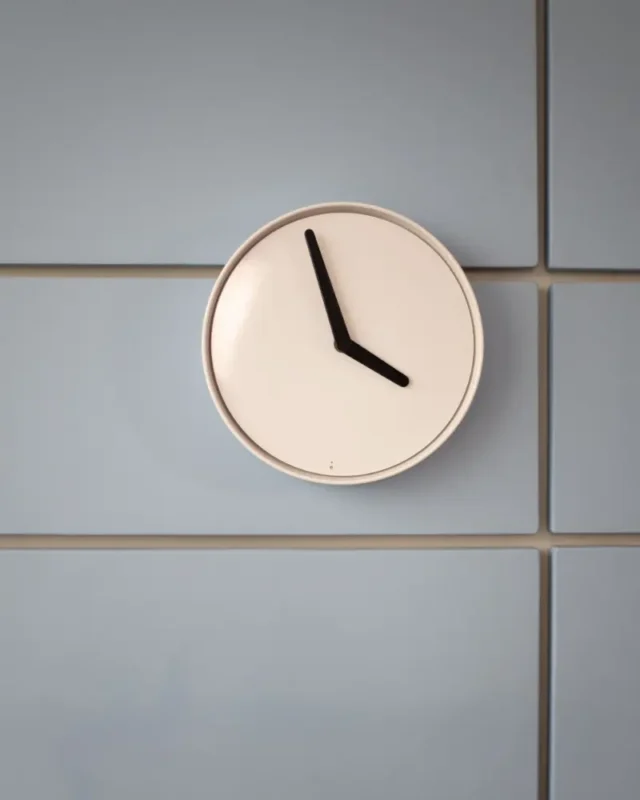 Halo minimal wall clock with a cream dial and bold black hands on a soft grey tiled wall