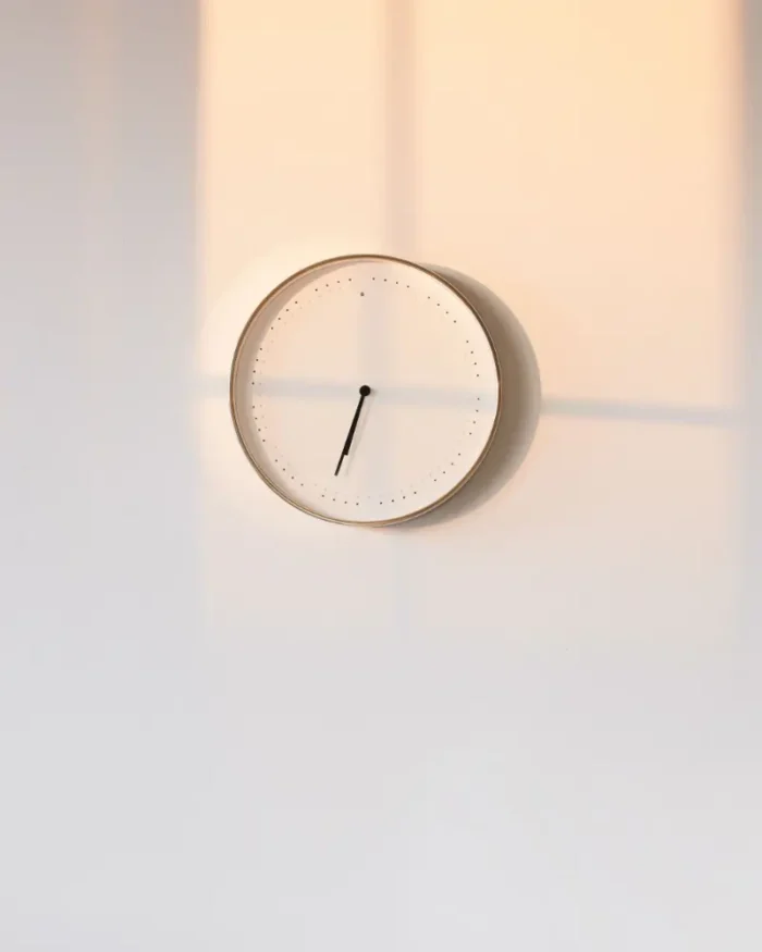 Halo minimal wall clock on a white wall, catching warm evening light and soft shadows