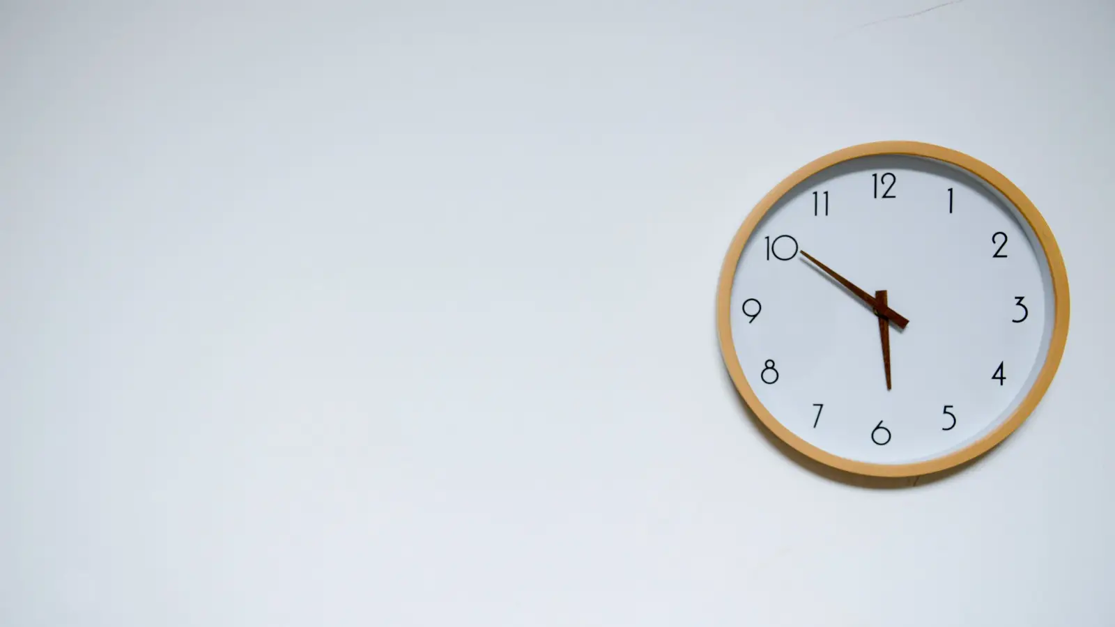 Minimal round wall clock with a warm wooden frame hanging on a bright white wall