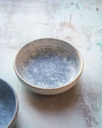 Terra stoneware bowl with a speckled blue reactive glaze on a rustic surface