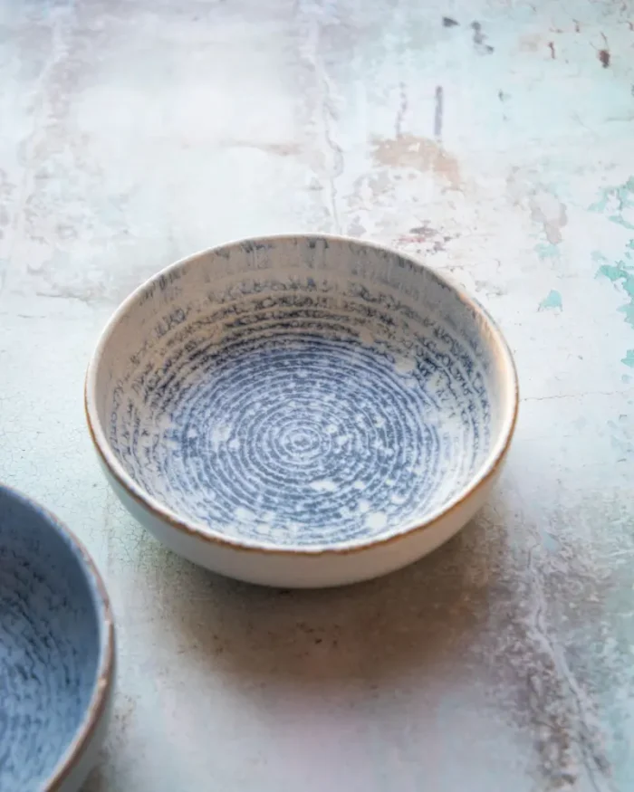 Terra stoneware bowl with a speckled blue reactive glaze on a rustic surface