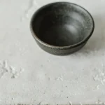 Terra reactive glaze stoneware bowl in a deep charcoal finish on a pale textured surface