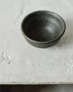 Terra reactive glaze stoneware bowl in a deep charcoal finish on a pale textured surface
