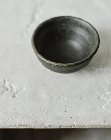 Terra reactive glaze stoneware bowl in a deep charcoal finish on a pale textured surface