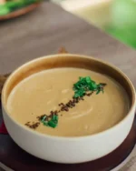 Terra stoneware bowl of creamy soup topped with fresh herbs on a wooden table