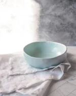 Terra stoneware bowl in a pale blue glaze resting on white linen in soft daylight