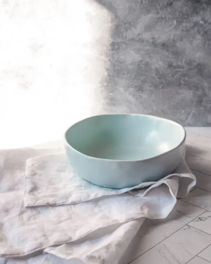 Terra stoneware bowl in a pale blue glaze resting on white linen in soft daylight