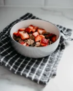 Terra stoneware bowl filled with strawberries and granola on a checked kitchen towel