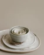 A nested stack of Terra stoneware bowls on a matching plate in soft neutral glazes