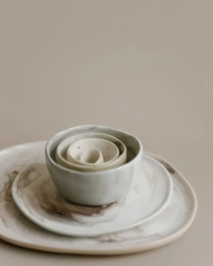 A nested stack of Terra stoneware bowls on a matching plate in soft neutral glazes