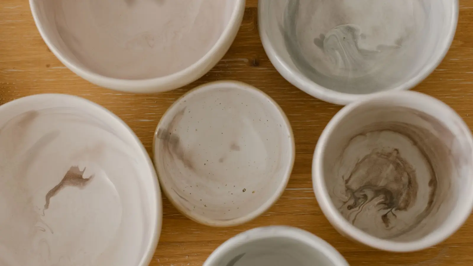 Handmade stoneware bowls in soft neutral glazes, seen from above on a wooden table